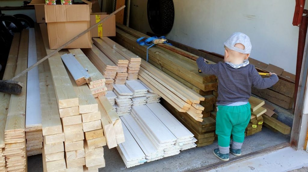 Autotalli täynnä puutavaraa ja lapsi mittamassa lautaa. 